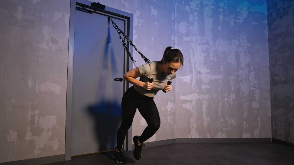 Девушка в отличной форме делает марщ в наклоне на тренировочных петлях