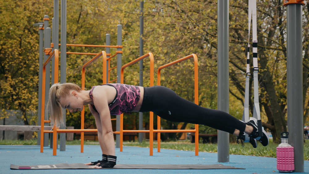 Девушка делает планку на тренировочных петлях