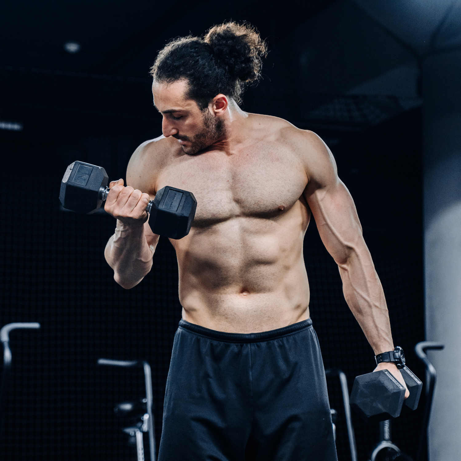 Мускулистый мужчина качает бицепс с гантелей